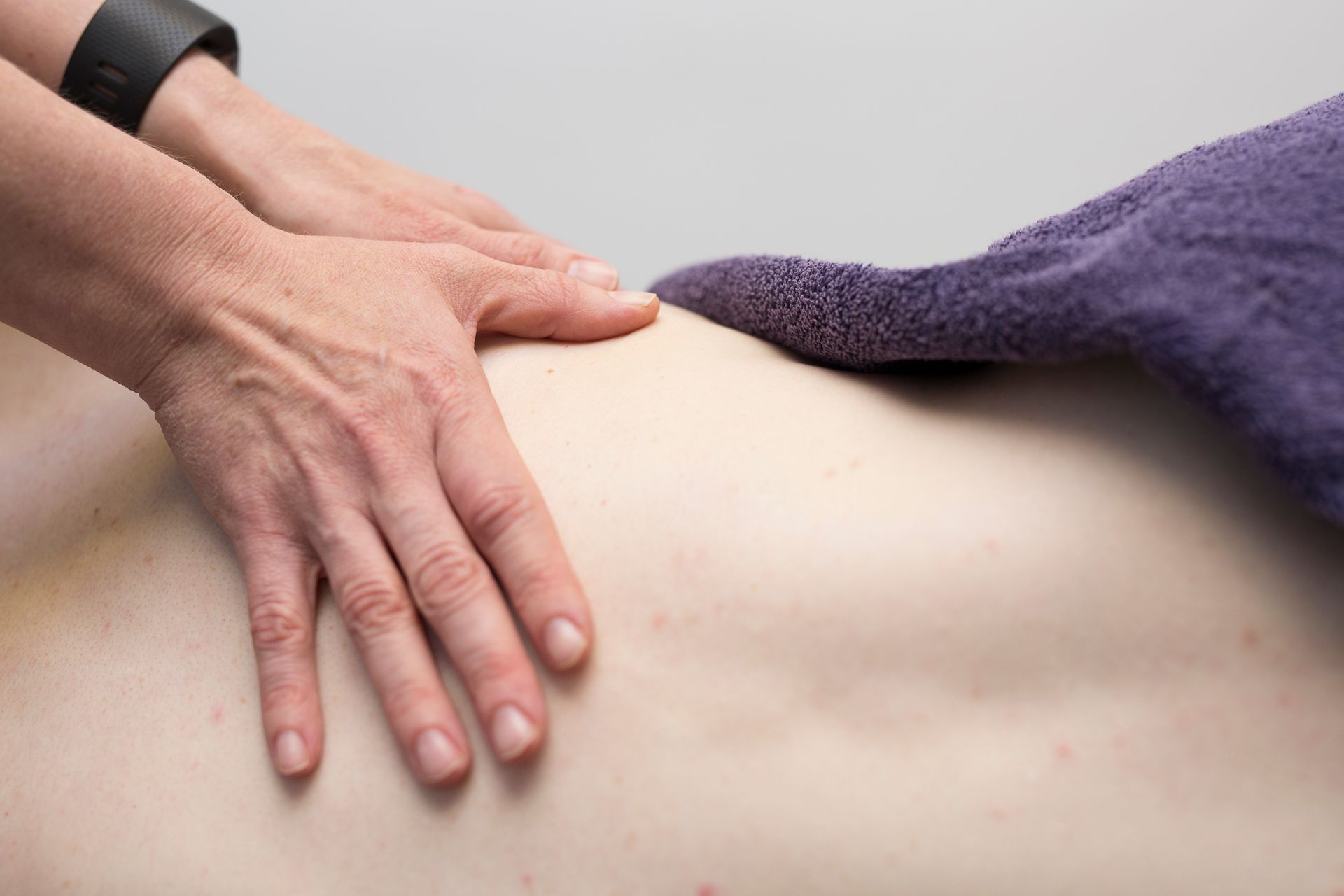 Hands massaging a person's back, next to a purple towel.