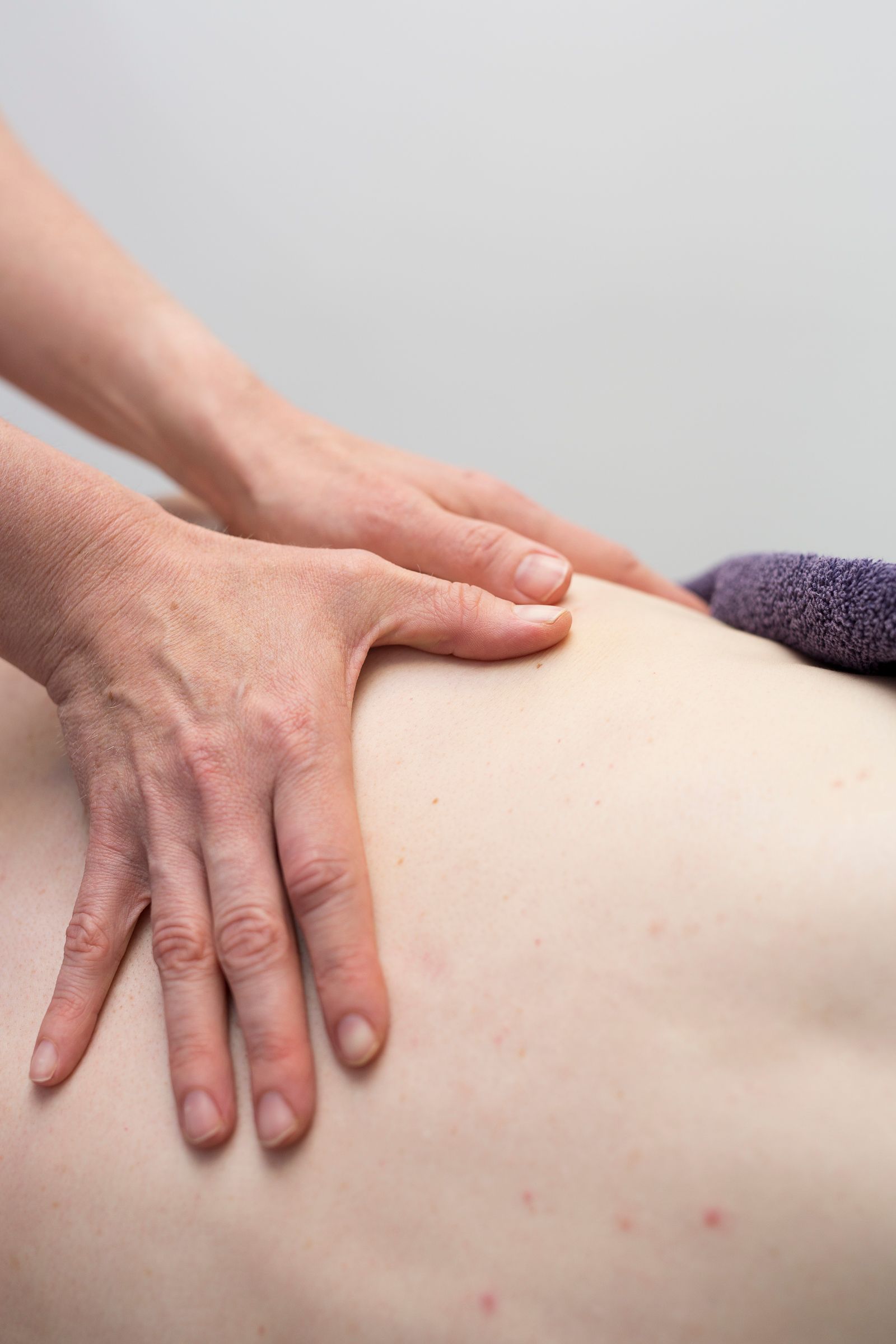 Hands massaging a person's lower back; neutral background, focused on physical therapy treatment.