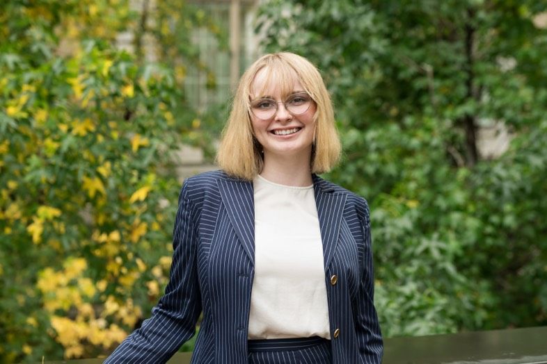 A woman wearing glasses is smiling in front of a plant and candles.