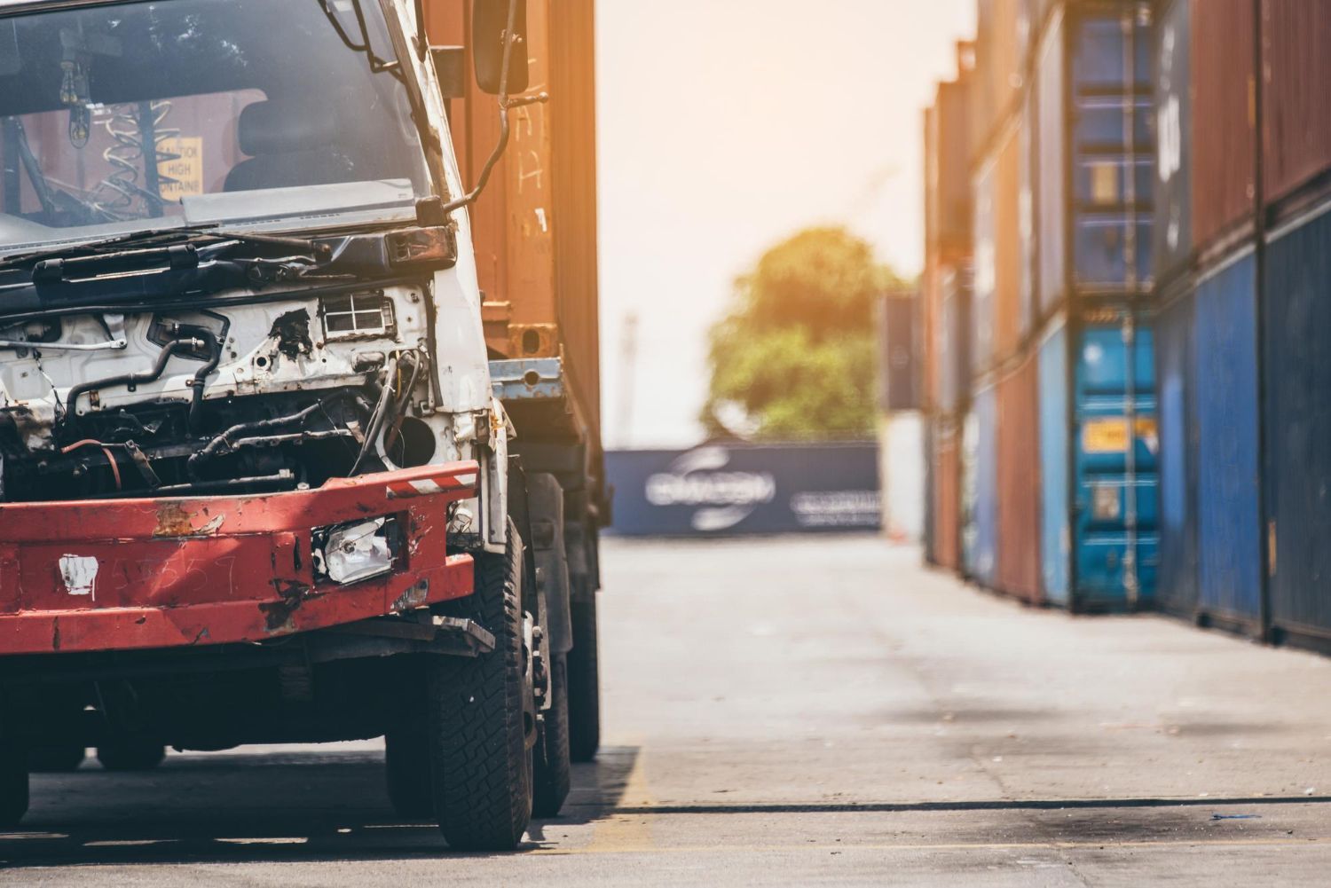A woman is kneeling down next to a damaged car and looking at her phone.
