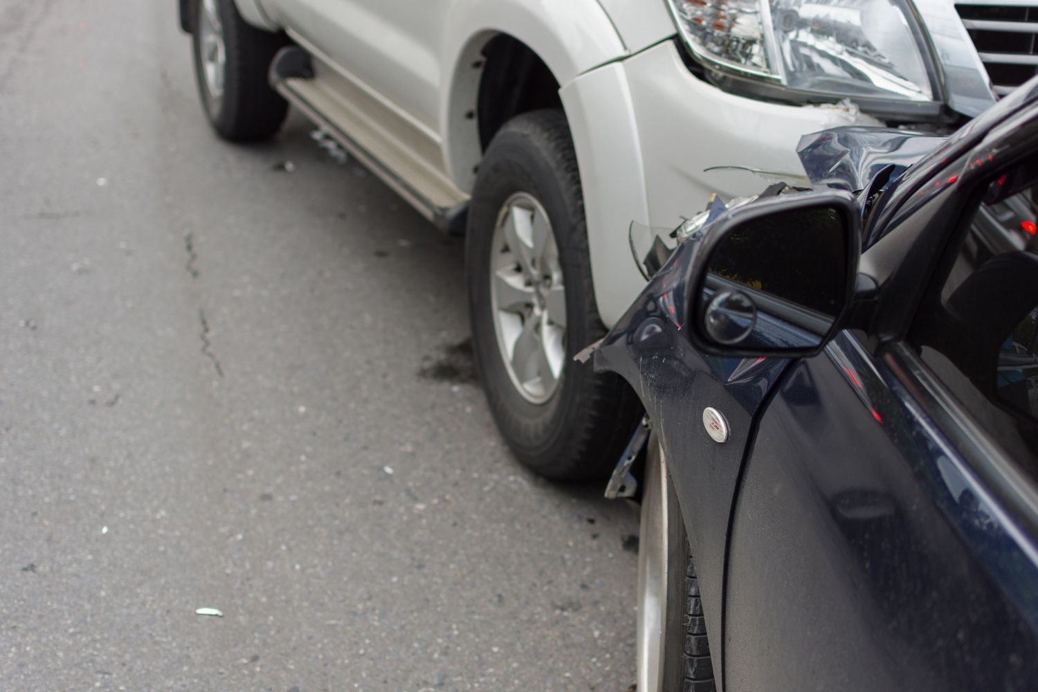 A woman is kneeling down next to a damaged car and looking at her phone.