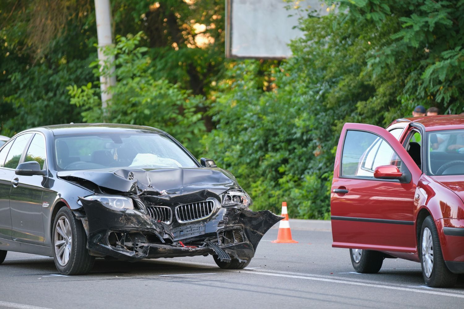 A woman is kneeling down next to a damaged car and looking at her phone.