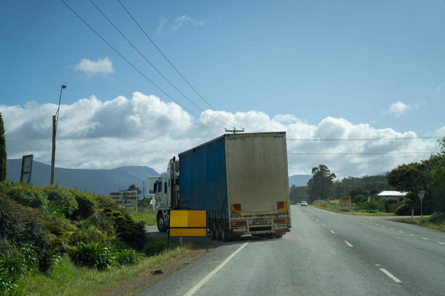 A woman is kneeling down next to a damaged car and looking at her phone.