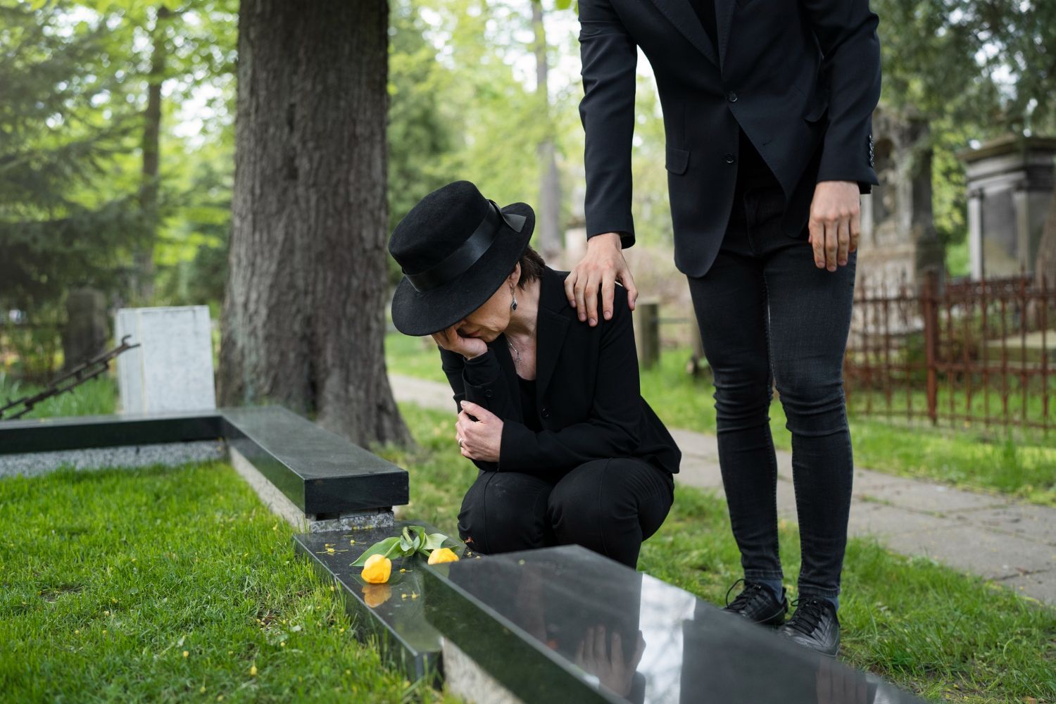 A man and a woman are kneeling at a grave in a cemetery.