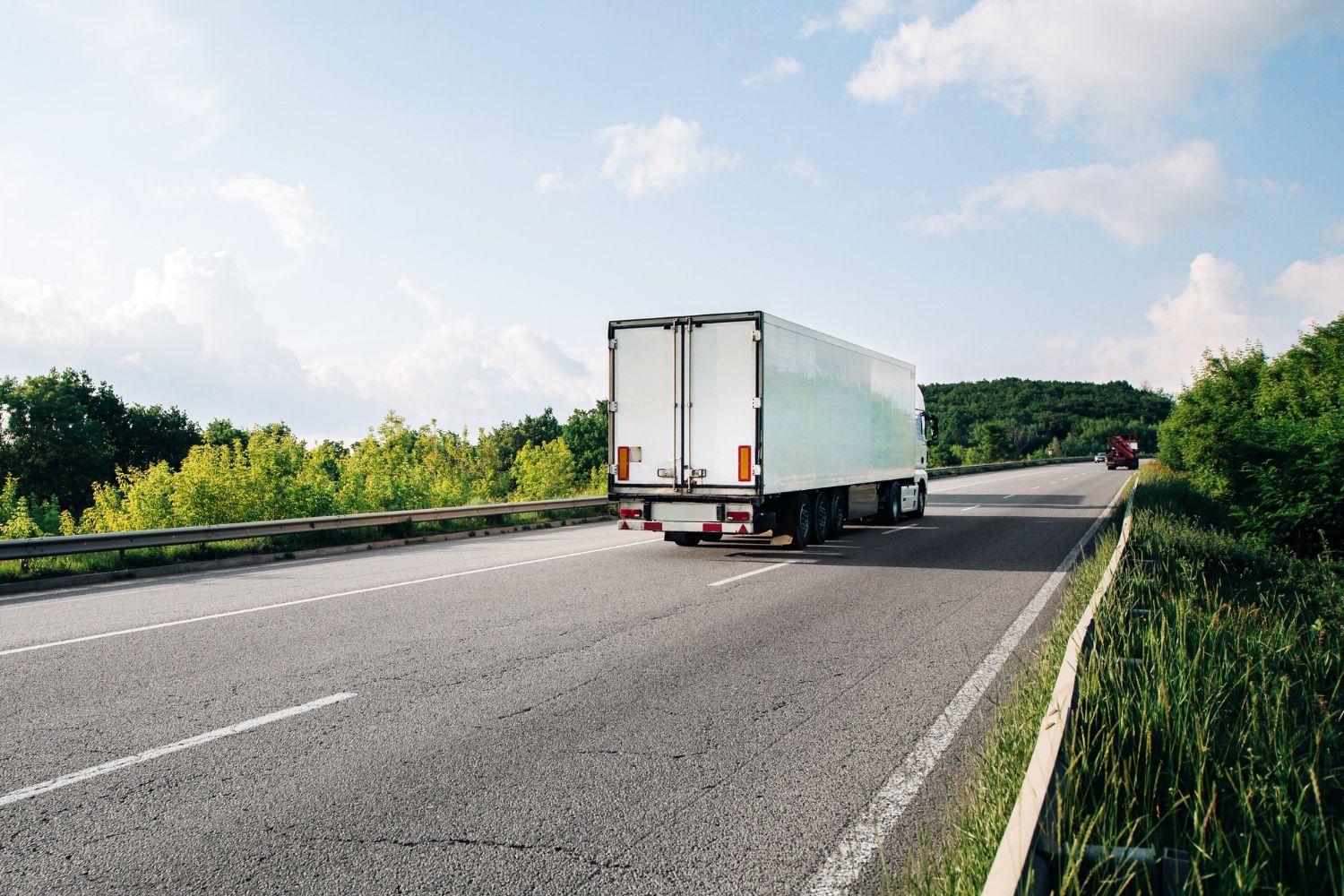 A woman is kneeling down next to a damaged car and looking at her phone.