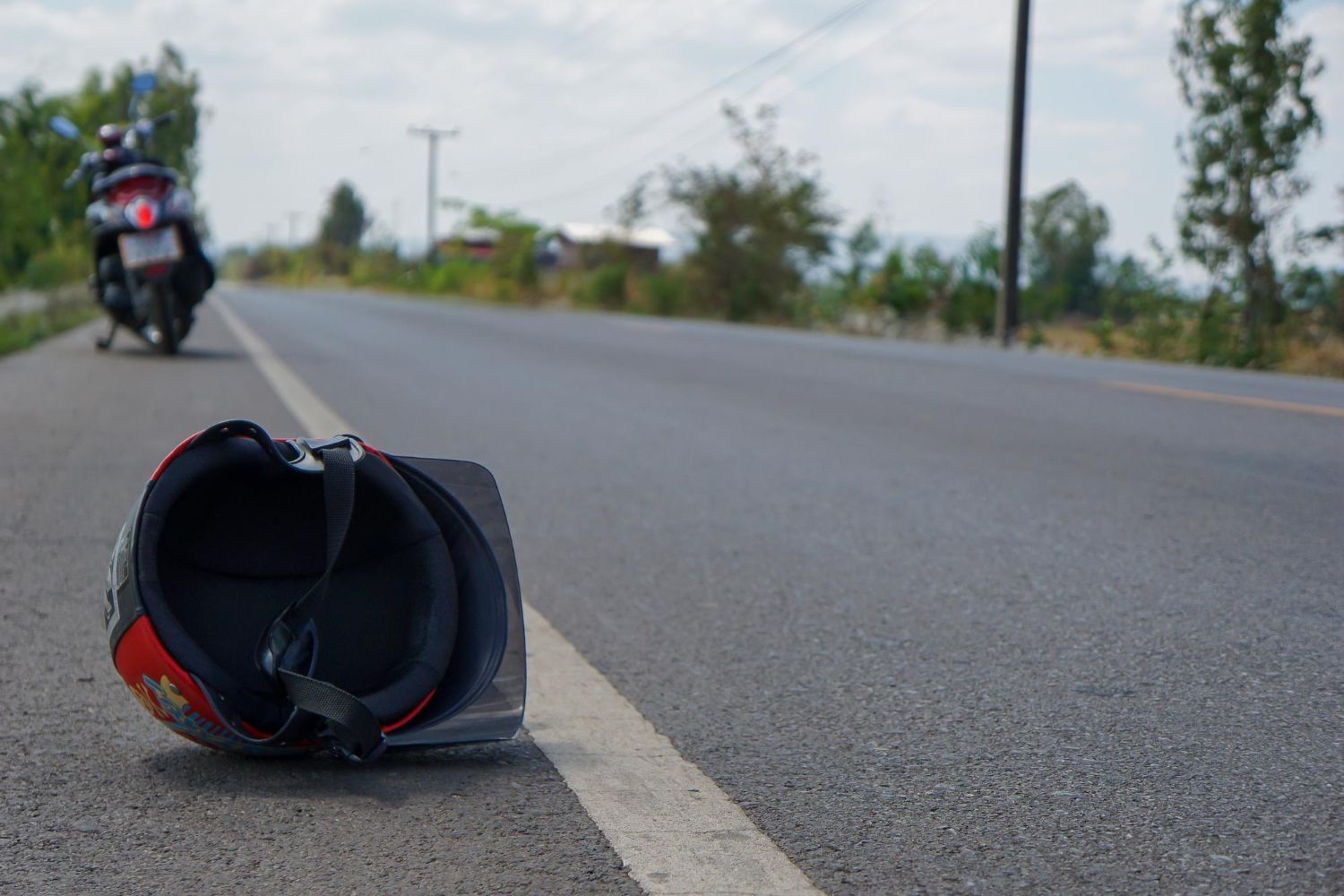 A woman is kneeling down next to a damaged car and looking at her phone.