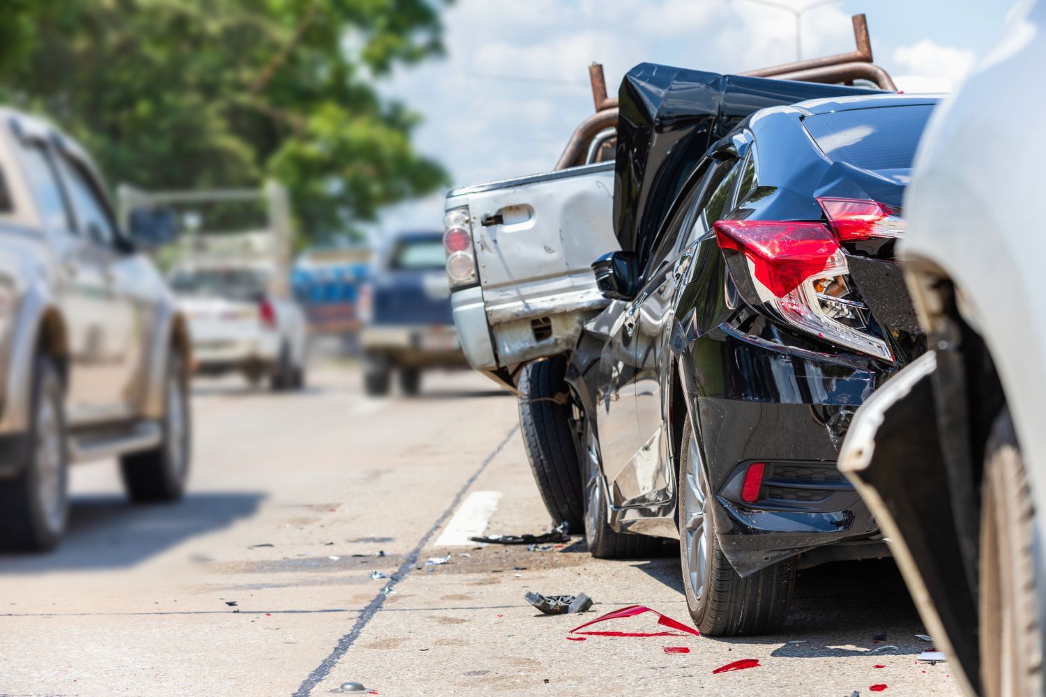 A woman is kneeling down next to a damaged car and looking at her phone.