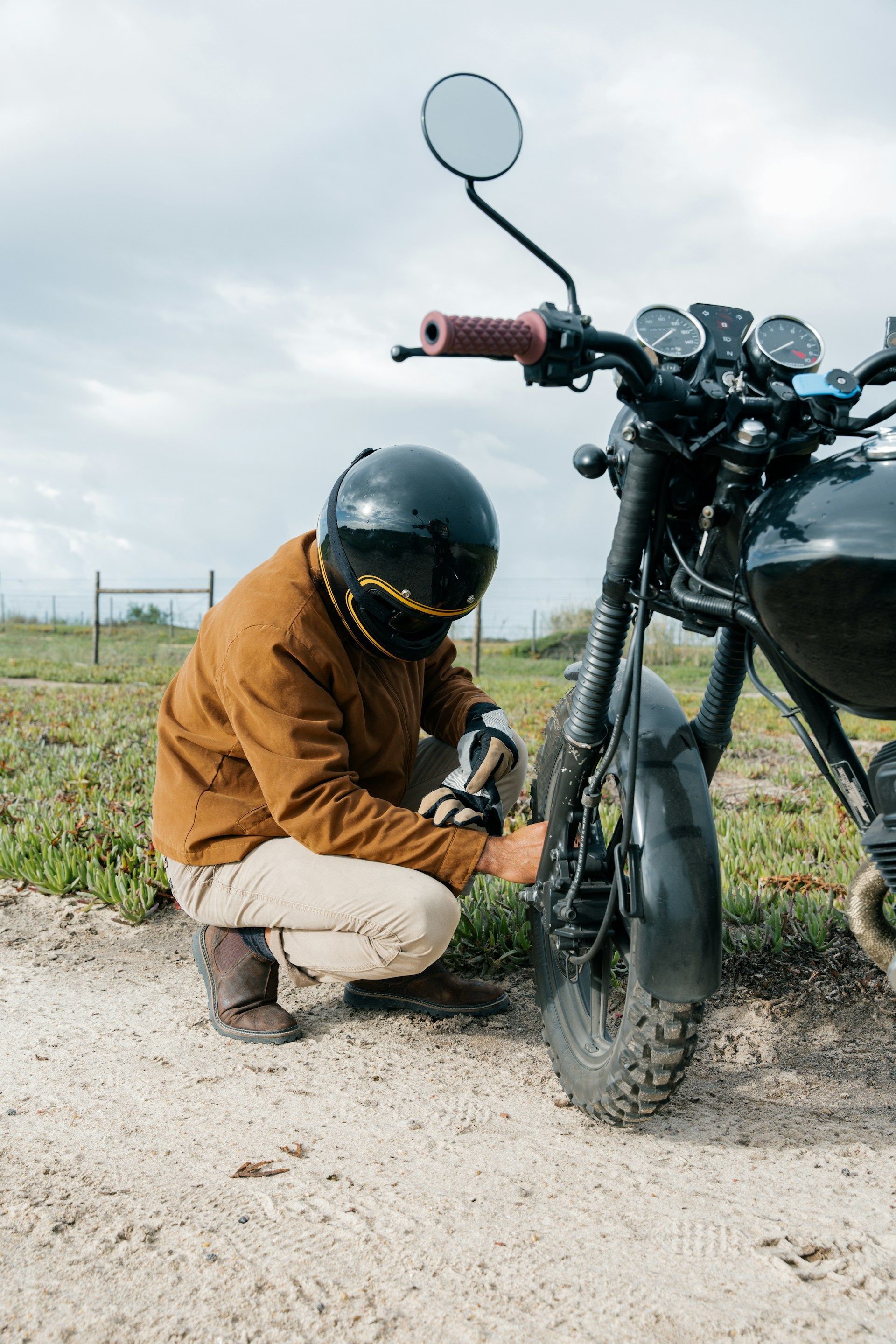 A woman is kneeling down next to a damaged car and looking at her phone.