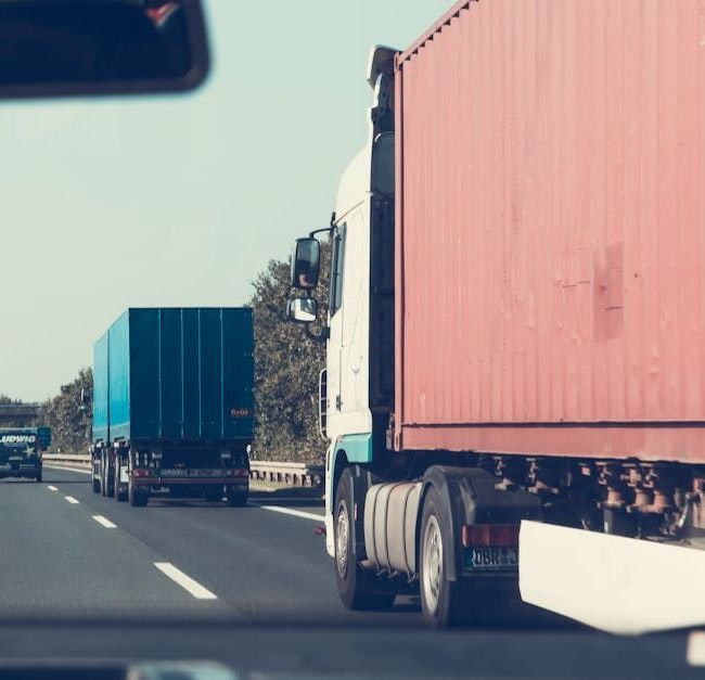 A red truck is driving down a highway next to a white truck.