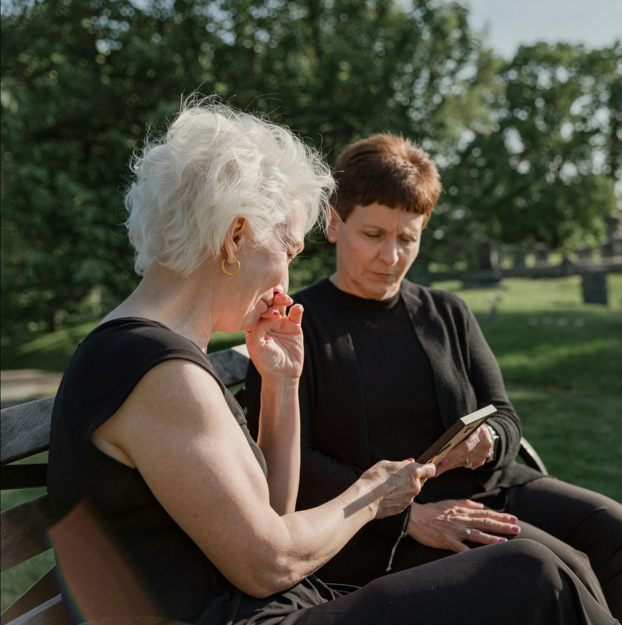 Two women are sitting on a bench looking at a book.