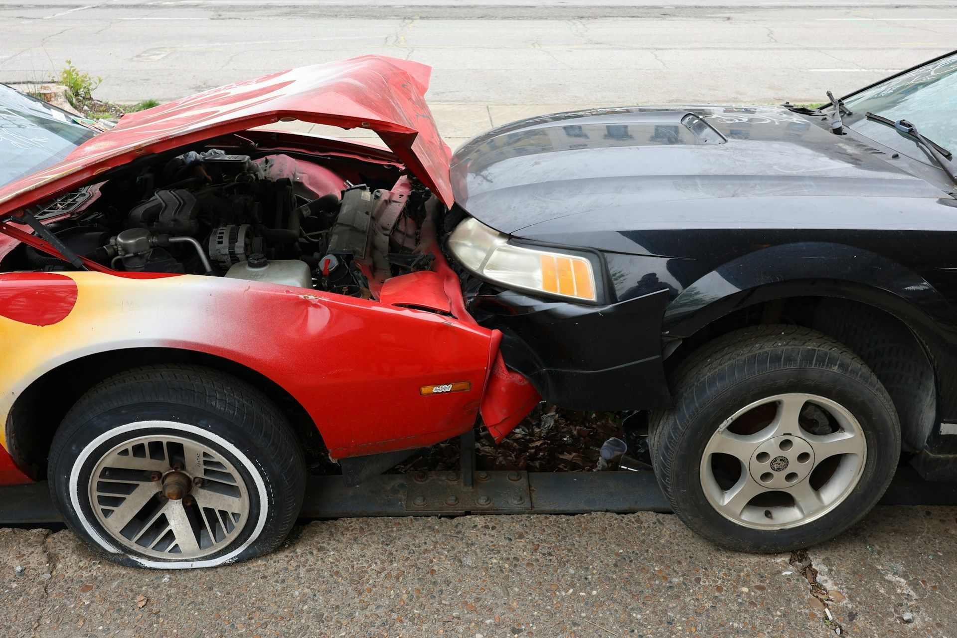A woman is kneeling down next to a damaged car and looking at her phone.