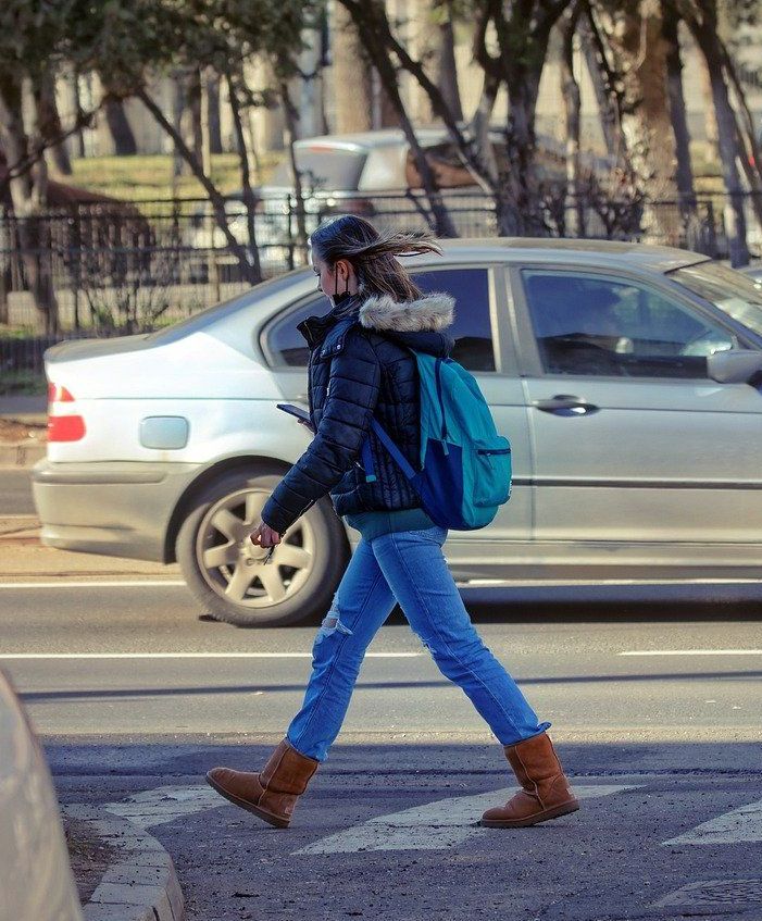 A woman with a backpack is crossing the street in front of a car