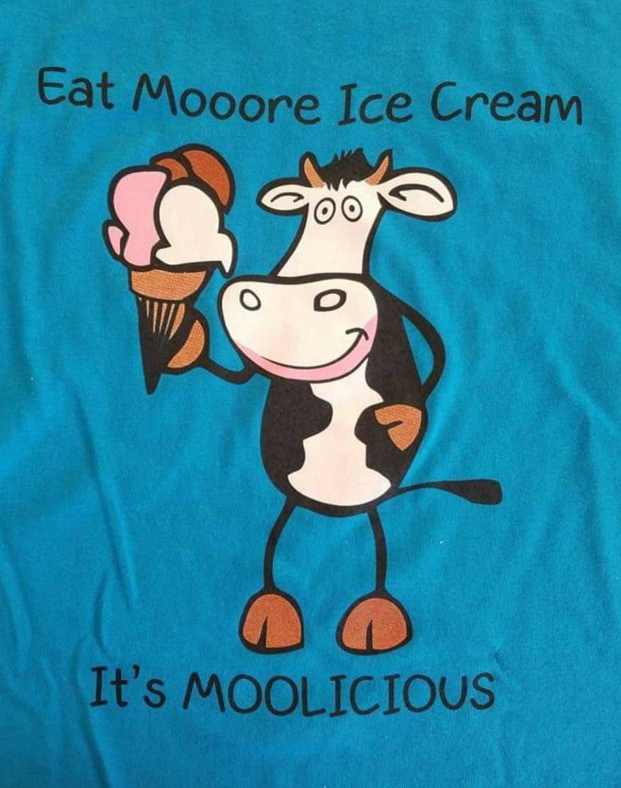 A blue shirt with a cow holding an ice cream cone that says eat mooore ice cream it 's moolicious