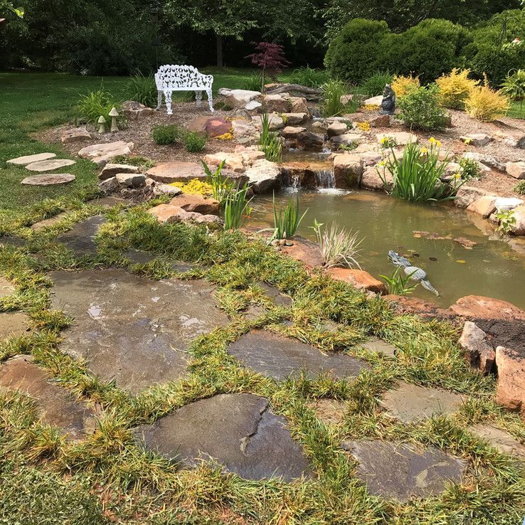 Garden pond with stepping stones, water plants, and a white bench in the background