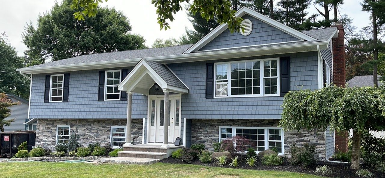 A large blue house with a stone facade and a gray roof is sitting on top of a lush green lawn.