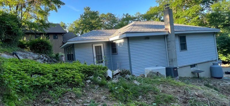 A small white house is sitting on top of a hill surrounded by trees.