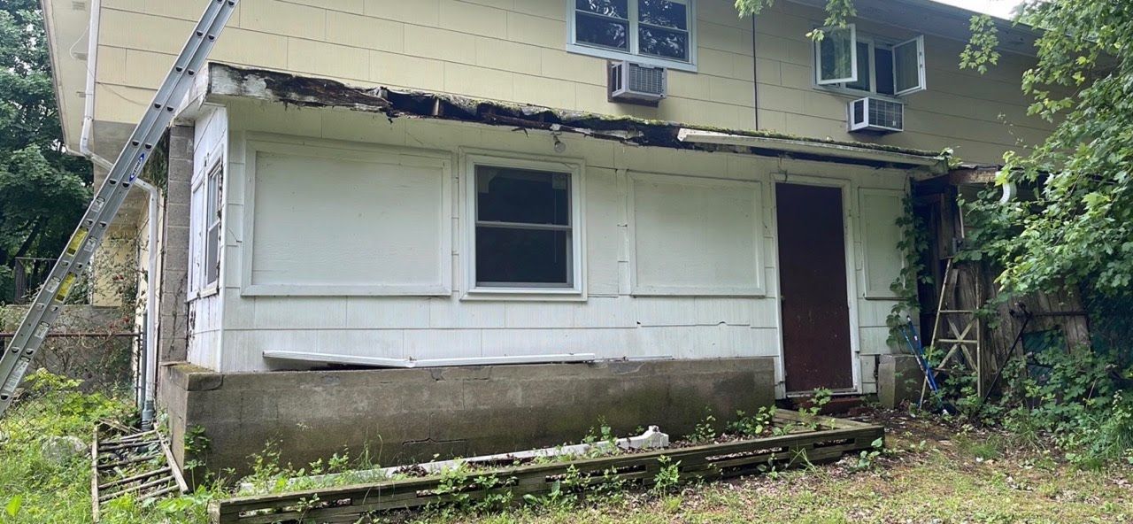 A white house with a brown door and a porch is sitting in the middle of a field.
