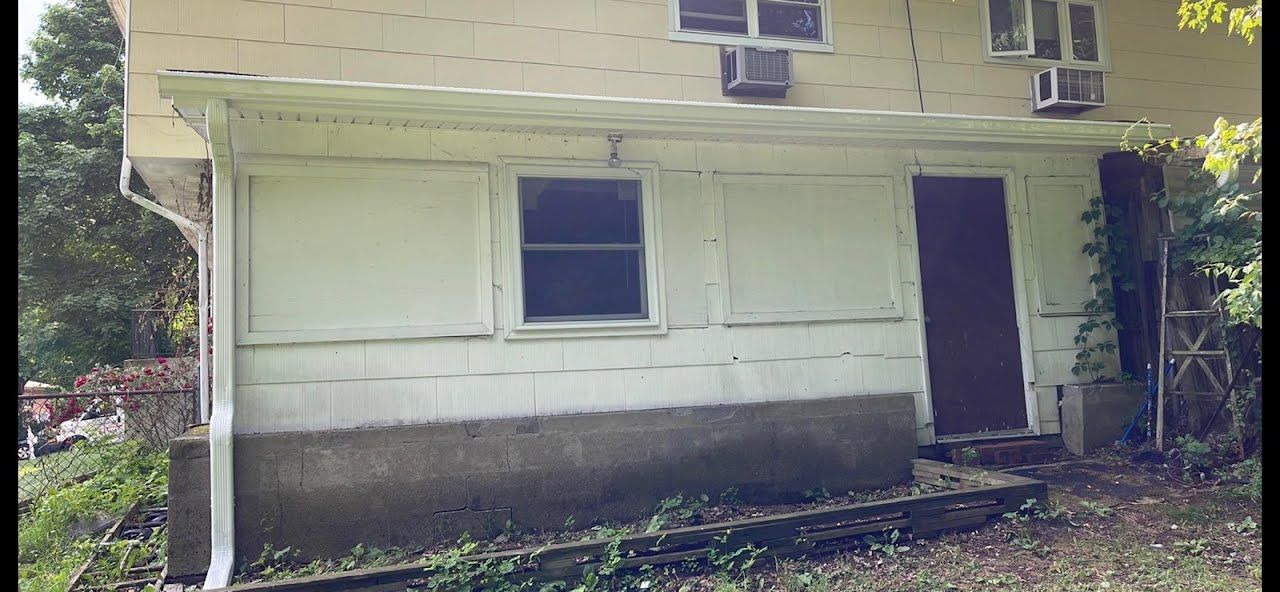 A white house with a brown door and windows is surrounded by trees.
