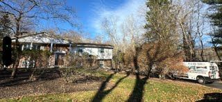 A white van is parked in front of a house surrounded by trees.