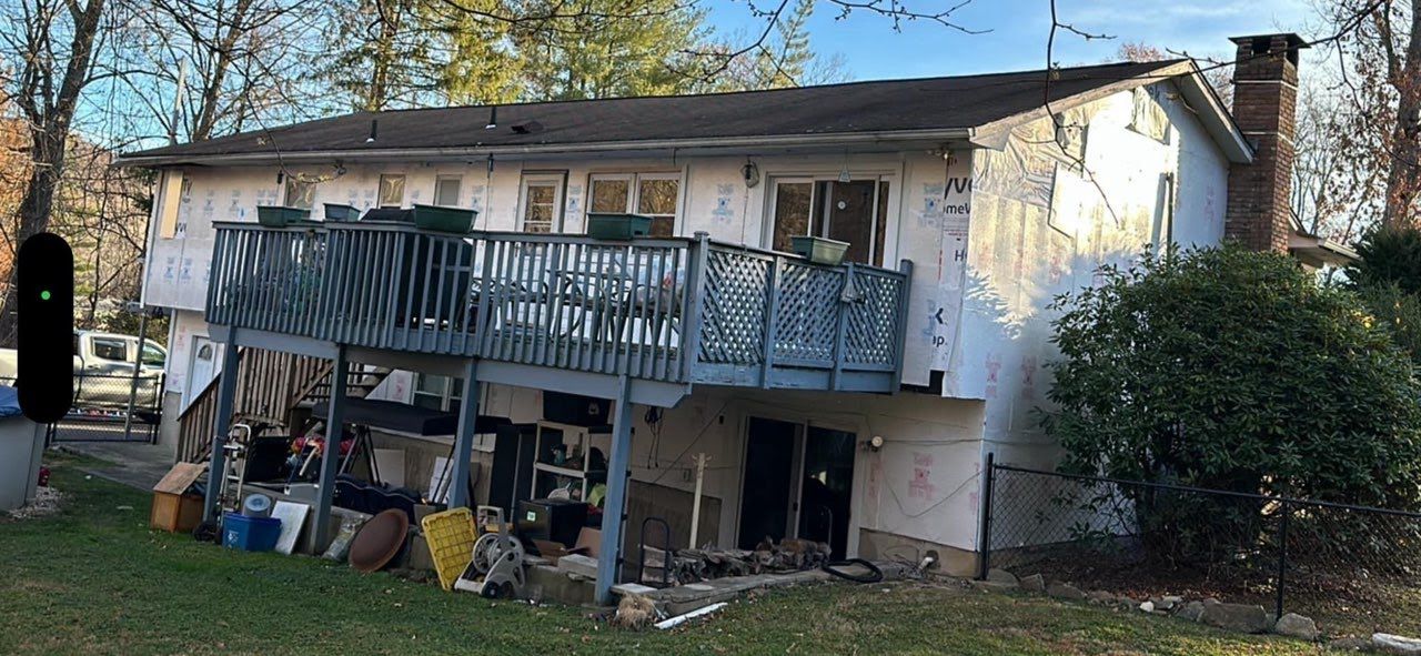 A house with a large deck and a lot of junk in the backyard.