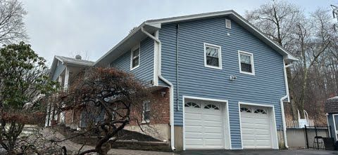 A blue house with two garage doors and a tree in front of it.