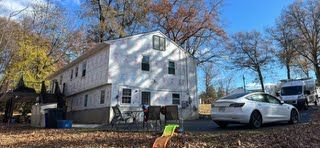 A white car is parked in front of a white house.