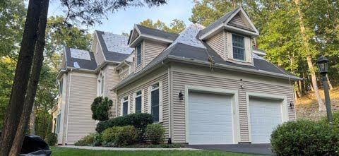 A large house with two garage doors is surrounded by trees.