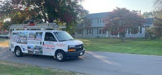 A white van is driving down a road in front of a house.