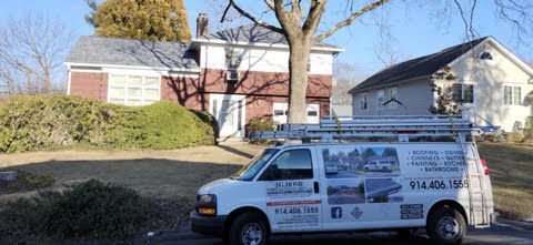A white van is parked in front of a brick house.