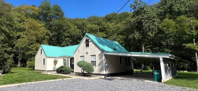 A white house with a green roof is surrounded by trees.