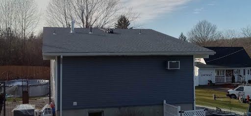 A small house with a gray roof is sitting in the middle of a field.
