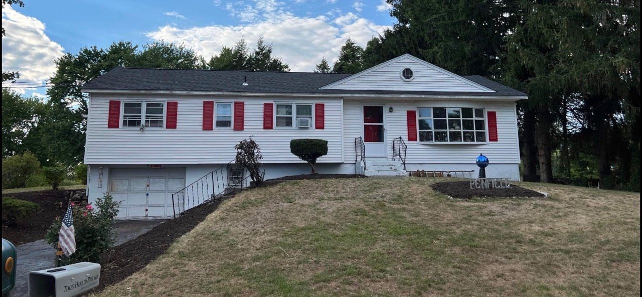 A white house with red shutters is sitting on top of a grassy hill.