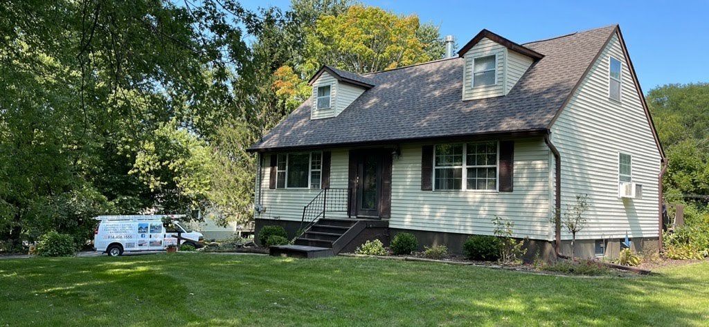 A white house with a gray roof and a white van parked in front of it.