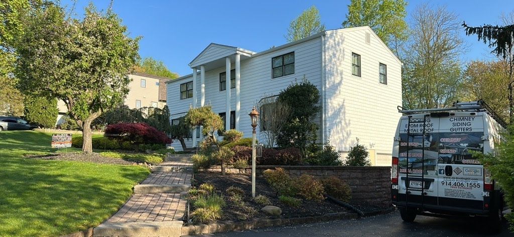 A white van is parked in front of a large white house.