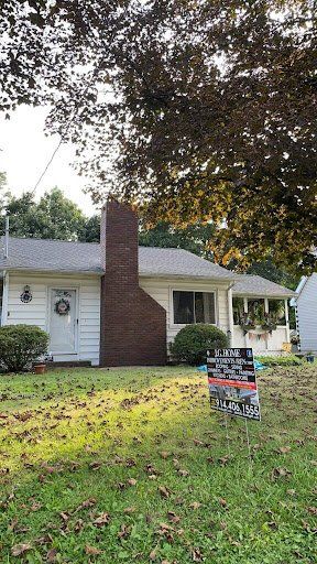 A white house with a brick chimney and a sign in front of it.