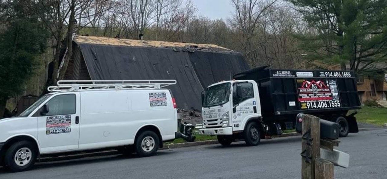 Two white vans and a dump truck are parked in front of a house.