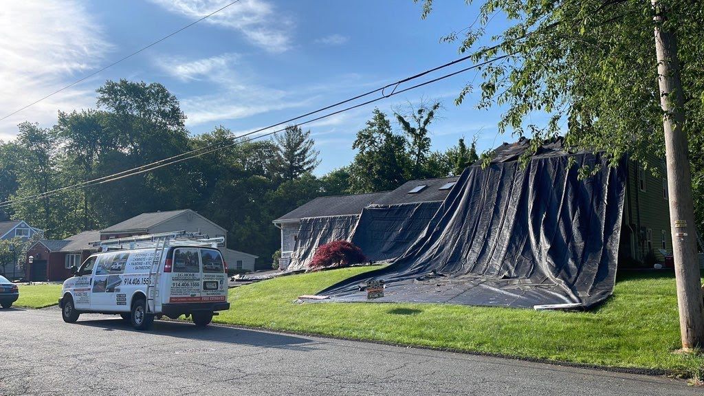 A white van is parked in front of a house with a tarp on the roof.