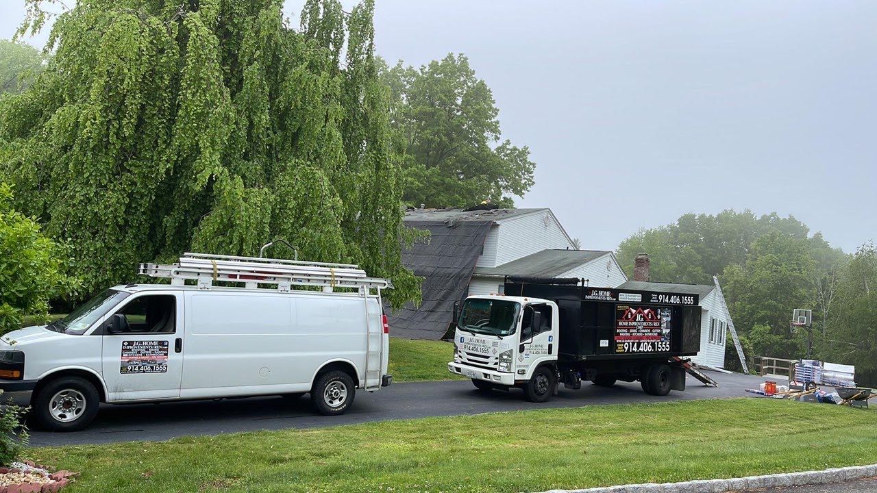 Two vans are parked in front of a house on a rainy day.