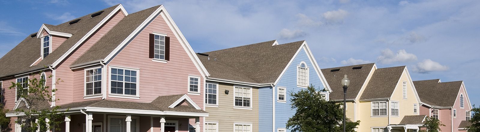 Suburban row of tan and blue townhouses with sloped roofs and white-trimmed windows on a sunny day