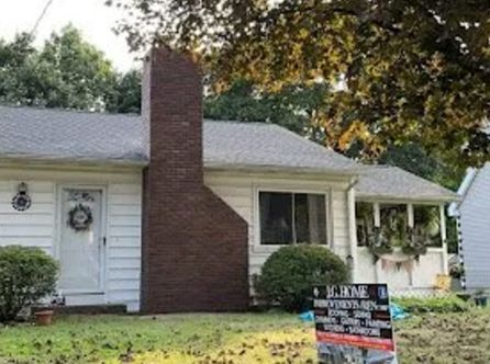 House with brick chimney and bushes. Sign in front of lawn.