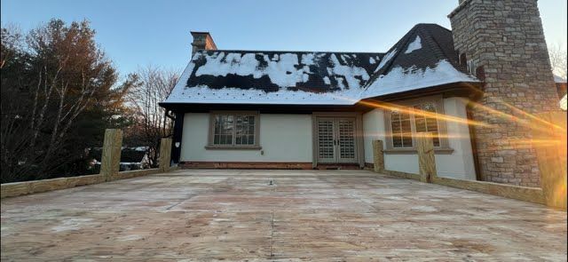 A house with snow on the roof and a driveway in front of it.