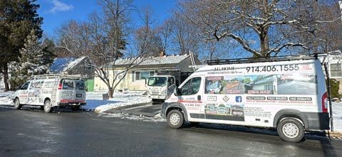 Three vans are parked in front of a house in the snow.