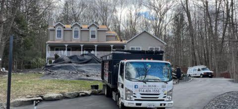 A dump truck is driving down a road in front of a house.