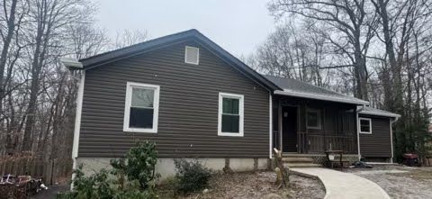 A small house with a walkway leading to it is surrounded by trees.