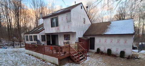 A large white house with a wooden deck in the snow.