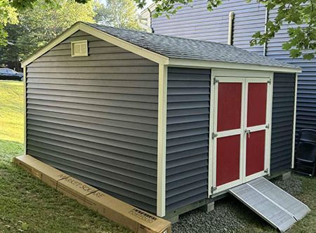 Gray shed with red doors, white trim, and a ramp.