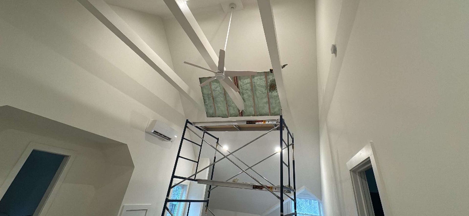 A person is standing on a scaffolding in a room with a ceiling fan hanging from it.