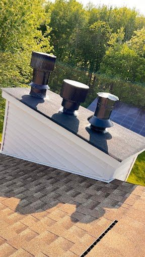 A roof with three chimneys on it and trees in the background.