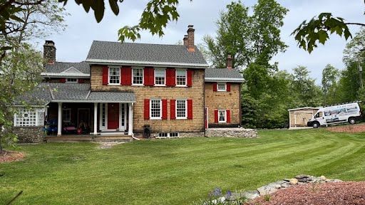 A large brick house with red shutters and a van parked in front of it.