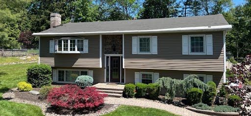 A large house with a gray roof and white shutters is sitting on top of a lush green hillside.